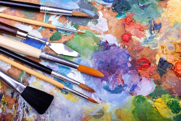 Paintbrushes arranged on a cork palette with multicolored acrylic paint strokes