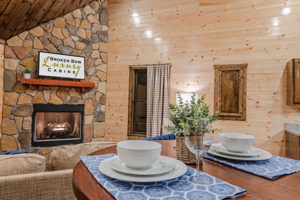 Cabin dining table set for two with stone fireplace and Broken Bow Luxury Cabins sign in background